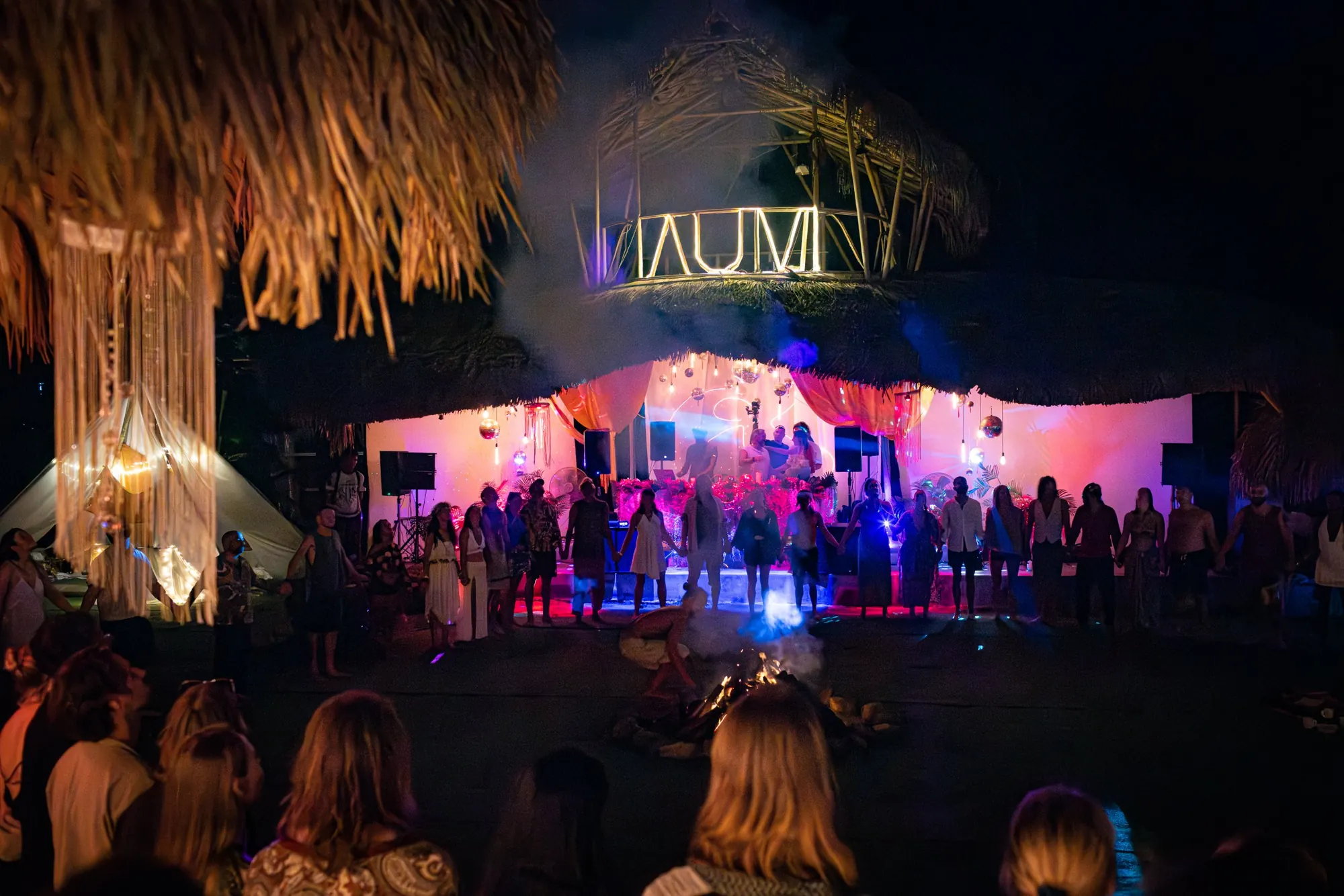 Dancers holding hands in a closing circle in front of the AUM stage
